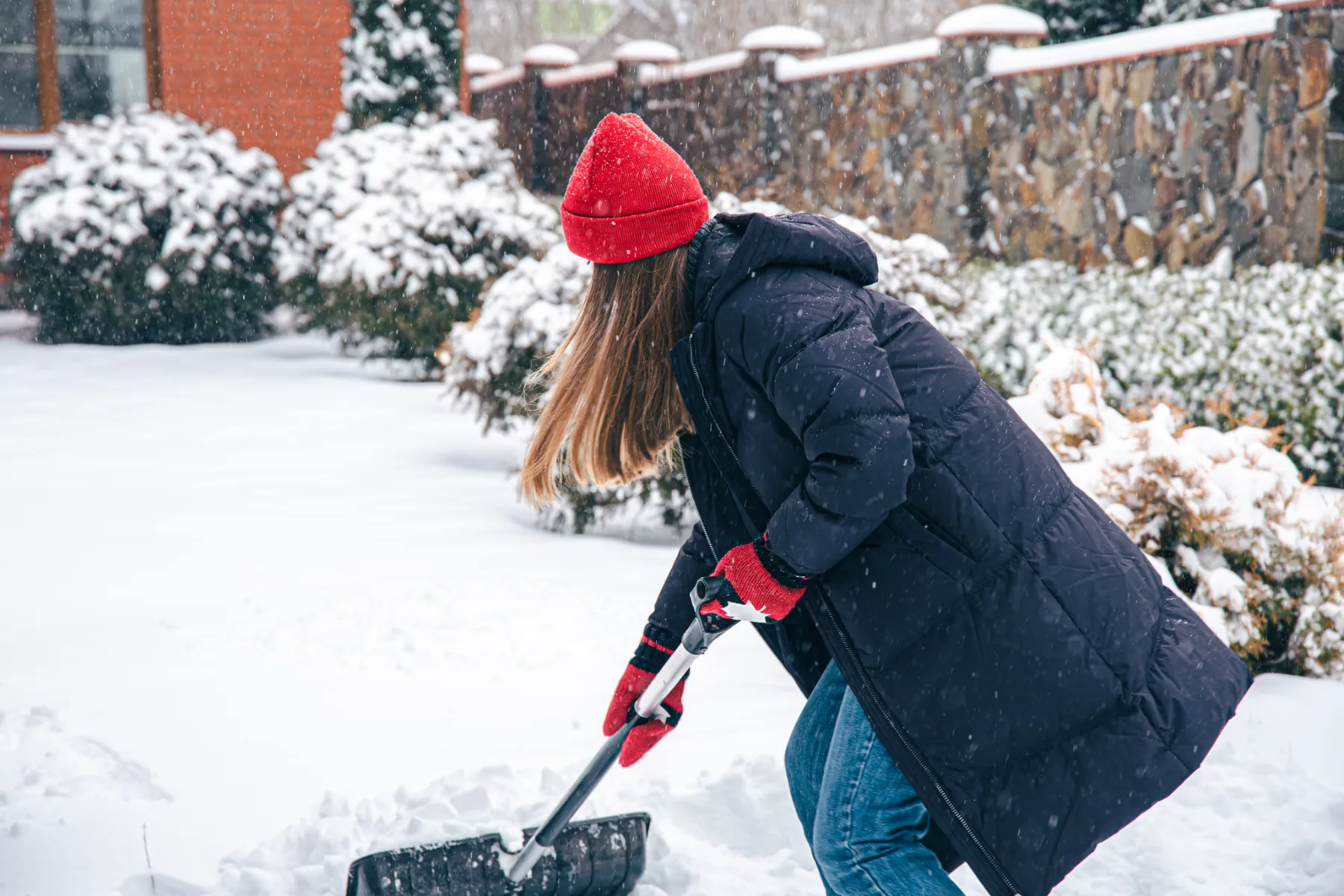 Frau räumt mit der Schneeschaufel Schnee vor dem Haus